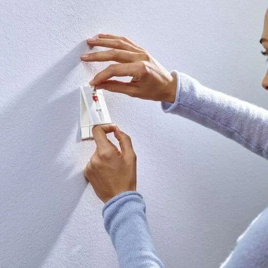 Tesa-2-mont2.jpg Kvinde viser, hvordan højdejustering med Tesa klæbesøm fungerer