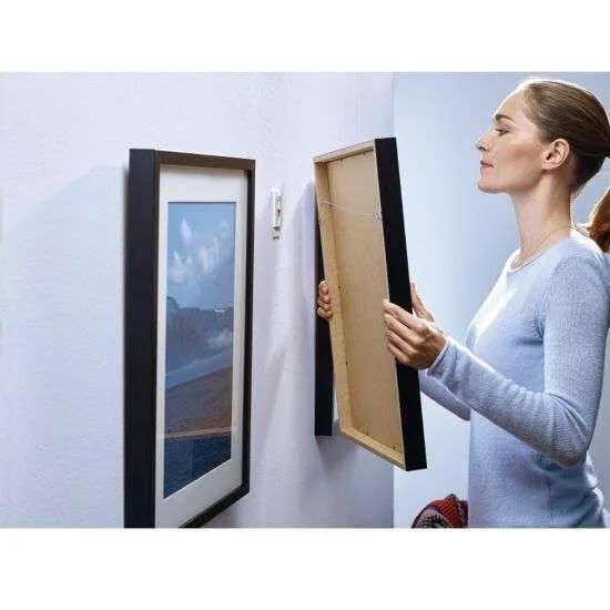 Tesa klæbesøm Kvinde viser, hvordan man hænger billeder på med Tesa klæbesøm til ophængning af billeder uden søm